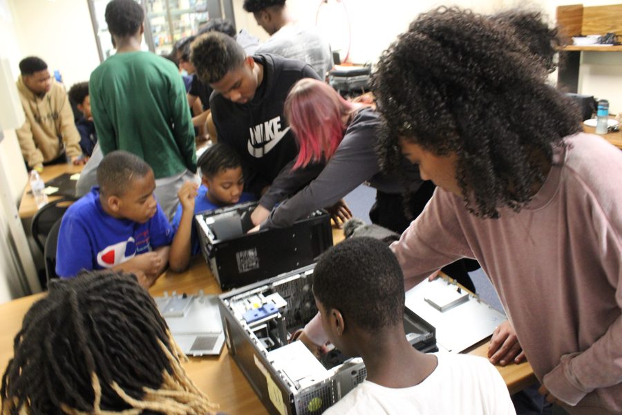 A crowded YTC work session: older students leaning in to guide younger students as they rebuild desktop computers together.